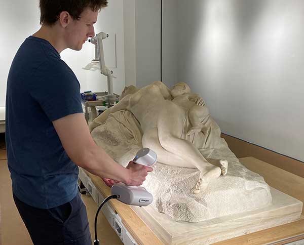 A WPI student standing next to the sculpture with a scanning device