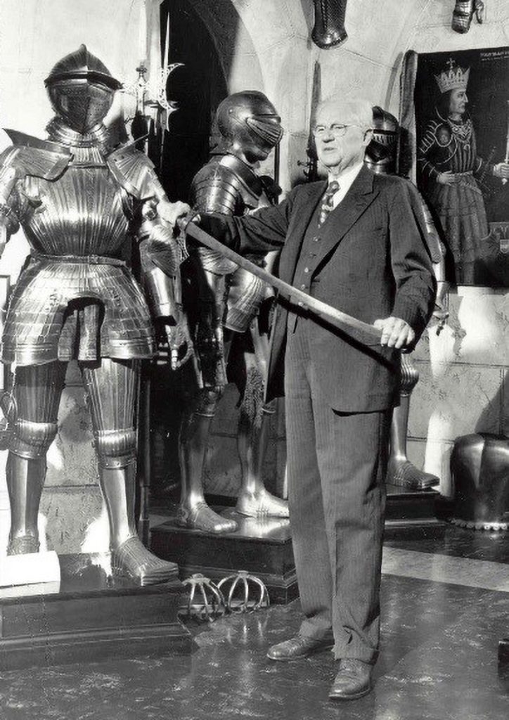 John Woodman Higgins wearing a suit and holding a sword, surrounded by objects from his collection