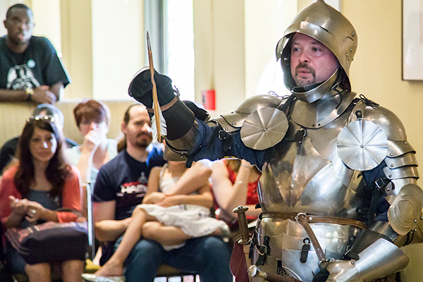 An educator dressed in knight's armor raises a sword during a demonstration