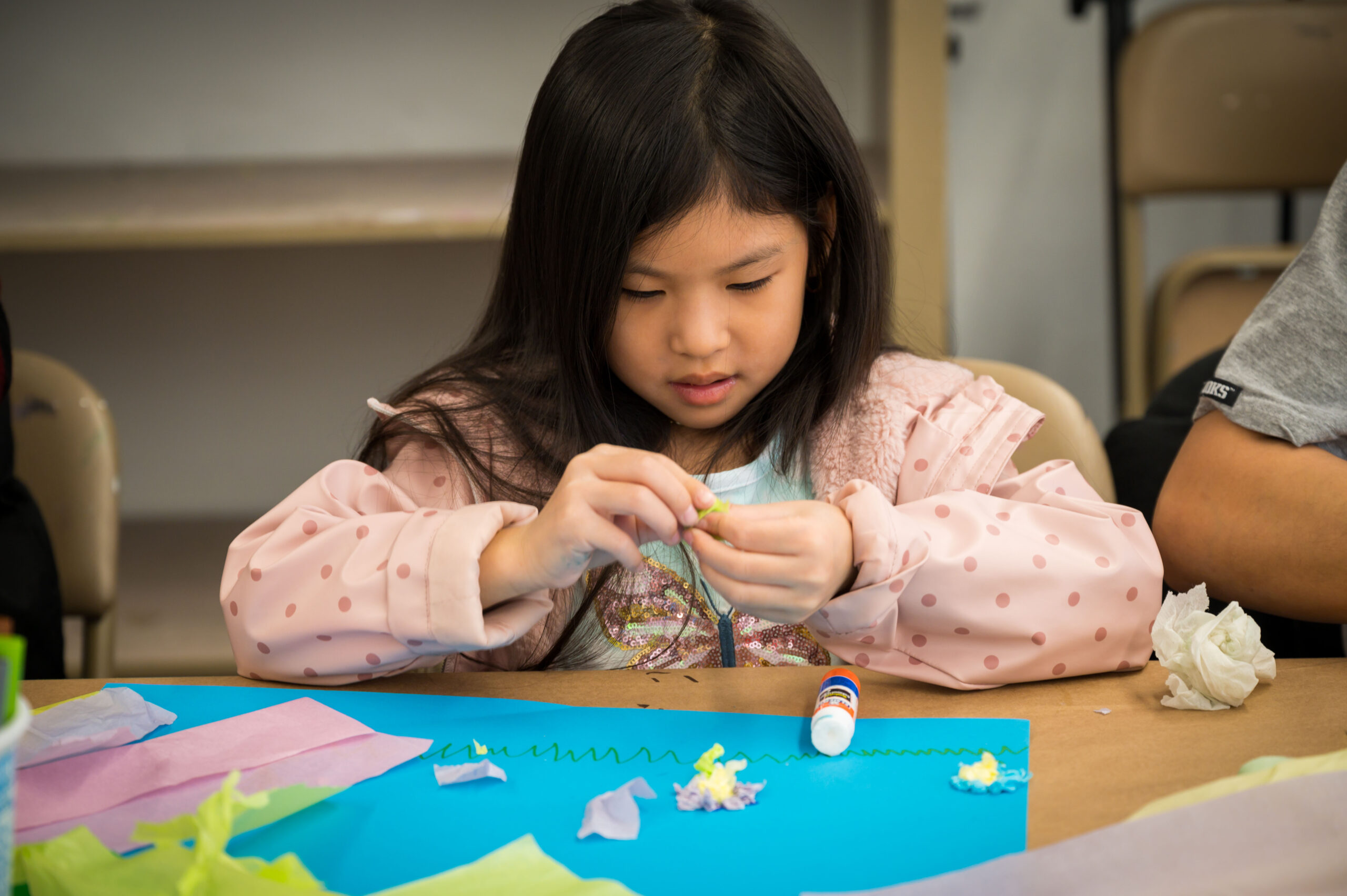 A girl sitting at a table making art with colored paper
