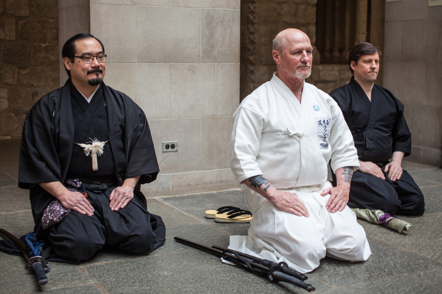 Three demonstrators dressed in samurai costume kneel together with their swords (katana) laid on the floor