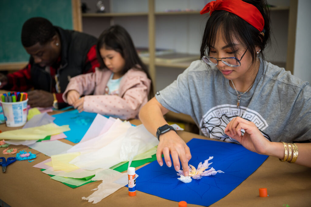 Two adults and a child sitting in a studio making art