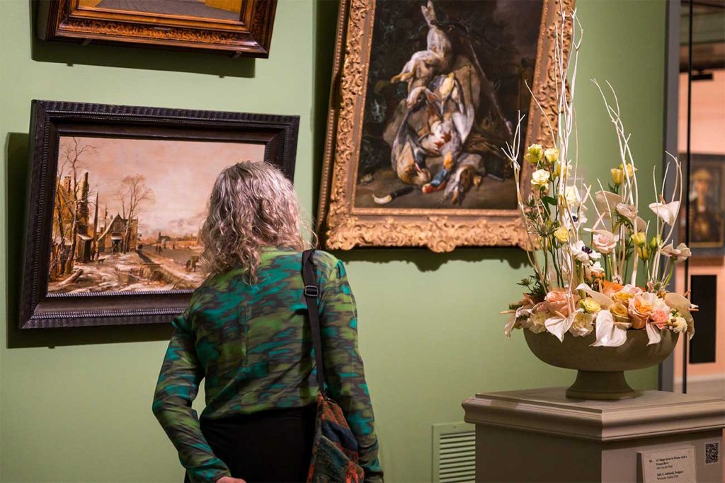 A visitor examining a painting with its floral interpretation in view