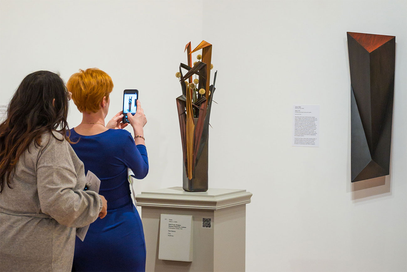 A visitor holds their phone up to take a photo of a floral interpretation