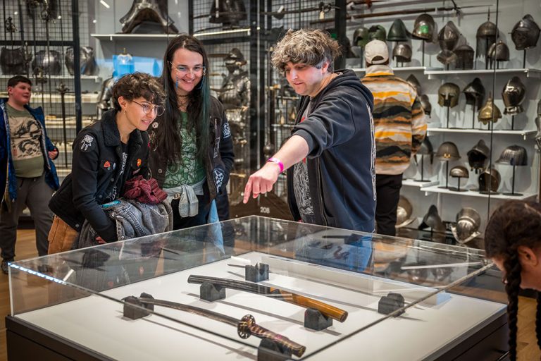 A group of visitors stand around a display case containing different types of sword