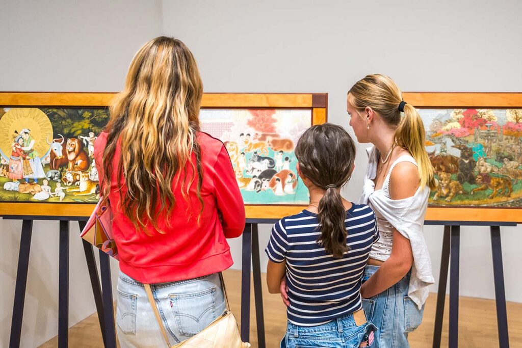 Three visitors gathered around one of the works in the exhibition 'Our Peaceable Kingdom'
