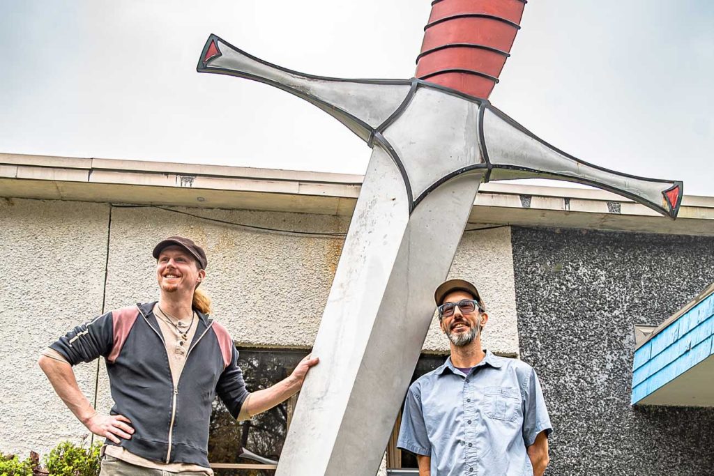 Local bladesmiths Joshua Swalec and Michael Coffey standing alongside a sculpture of a giant sword