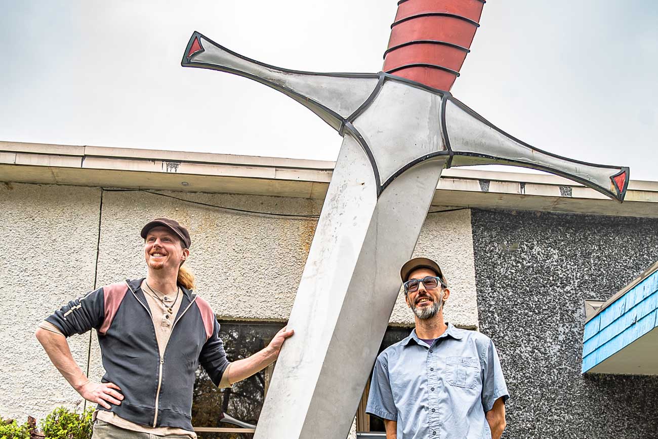 Local bladesmiths Joshua Swalec and Michael Coffey standing alongside a sculpture of a giant sword